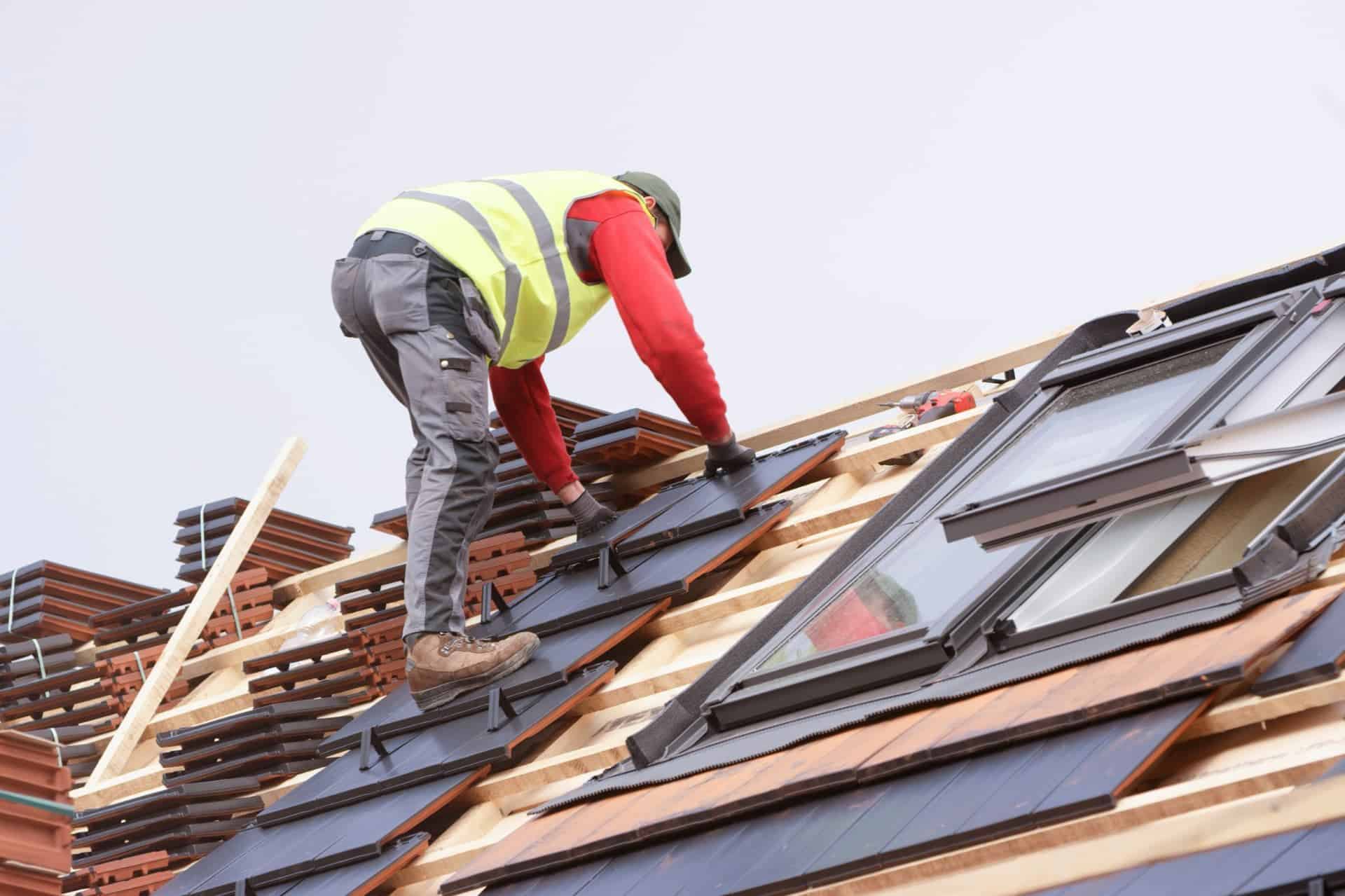 Roofer installing new roof tiles next to skylights