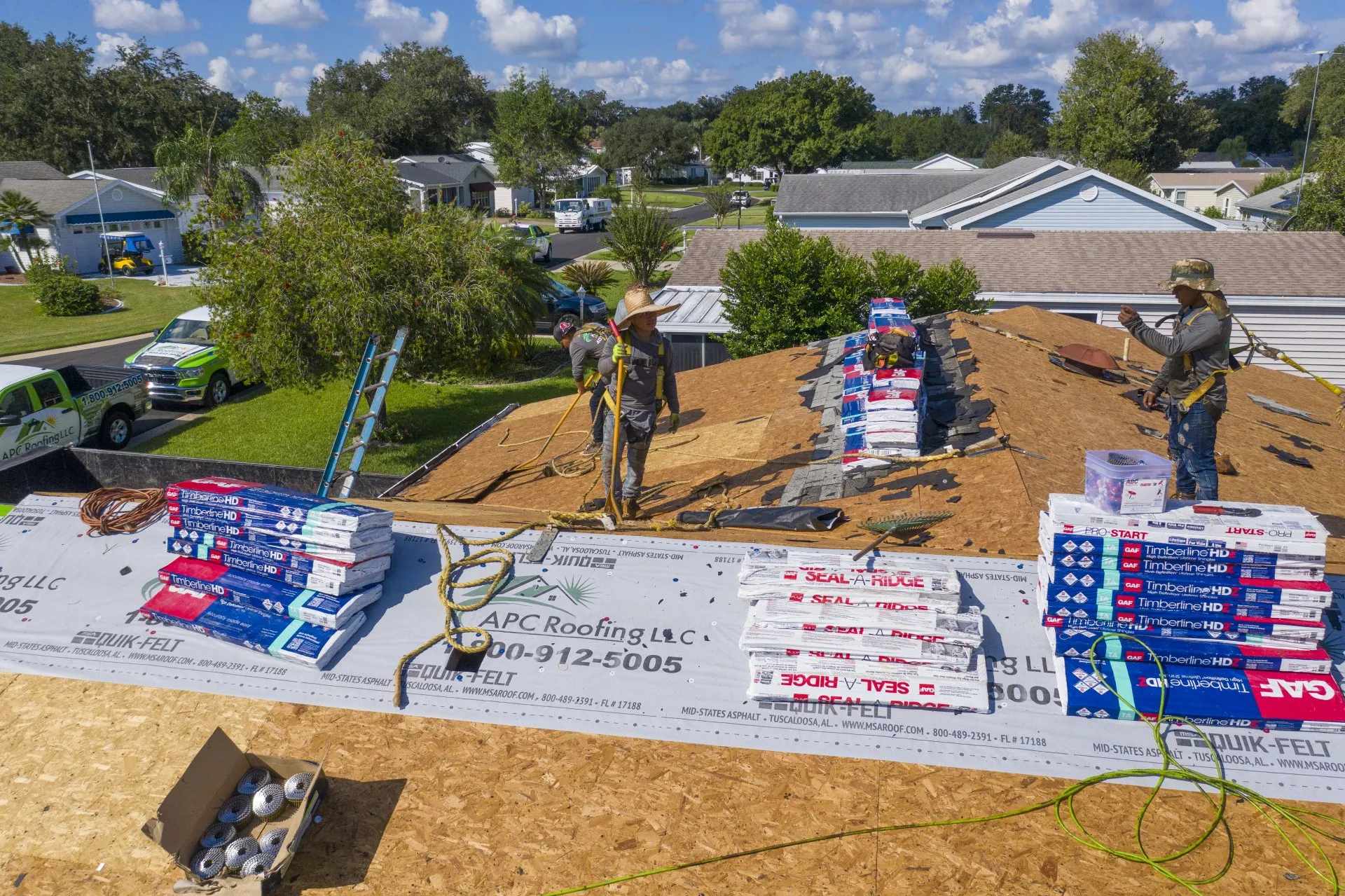 Roofers work on installing shingles on a residential roof, with stacks of roofing materials and safety equipment visible on the rooftop. Roofers work on installing shingles on a residential roof, with stacks of roofing materials and safety equipment visible on the rooftop.