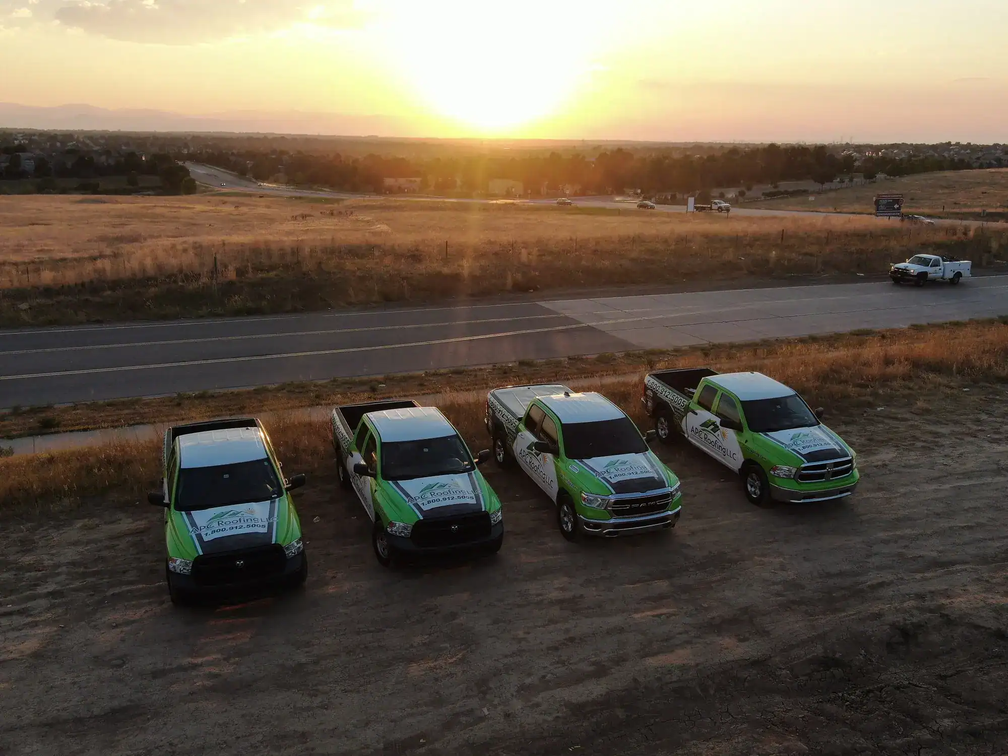 Roofing crew vehicles parked on site at sunset, ready for storm damage repairs and roof inspections.