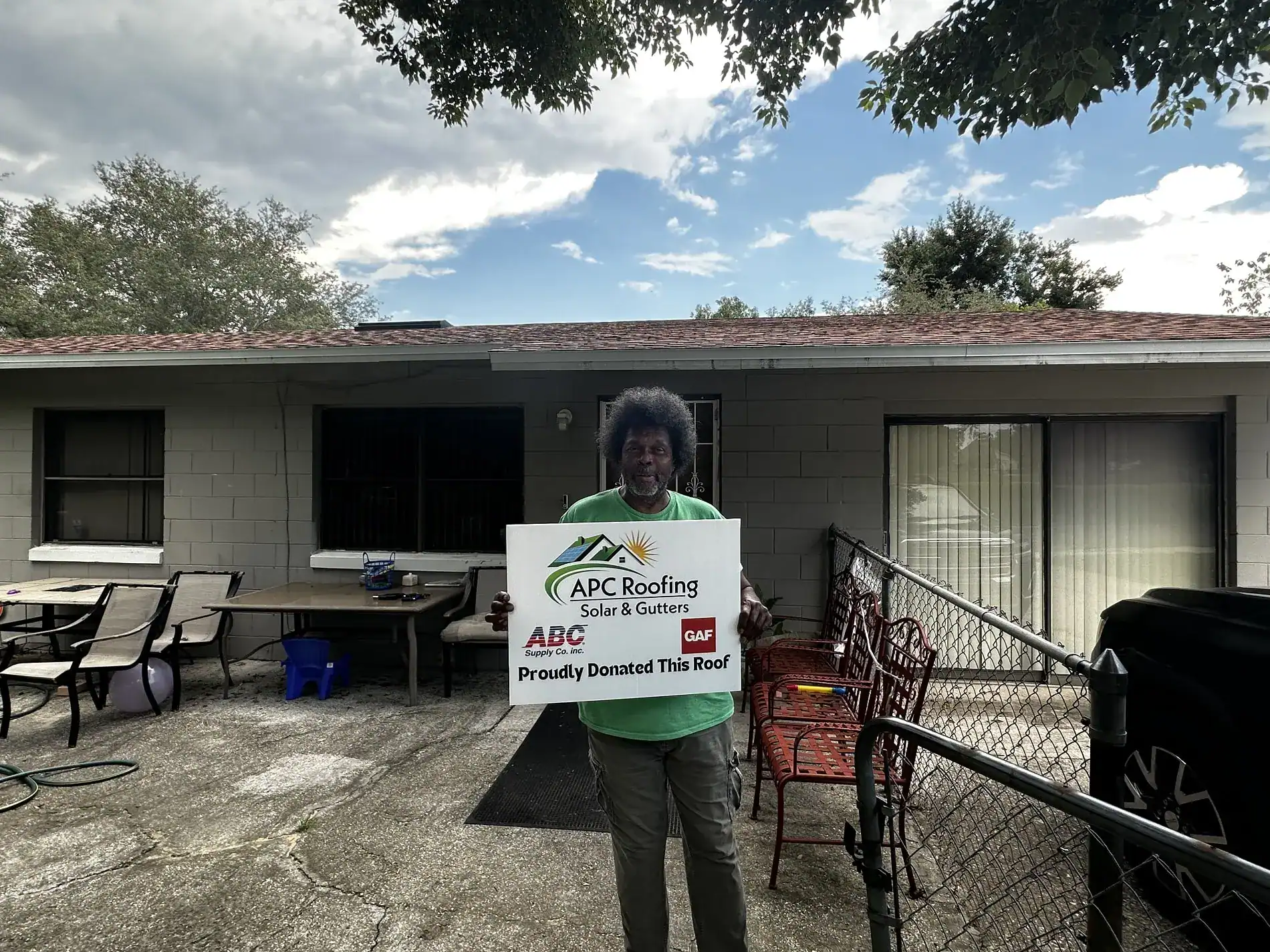 Roofing contractor APC Roofing team member holding a sign in front of a house.