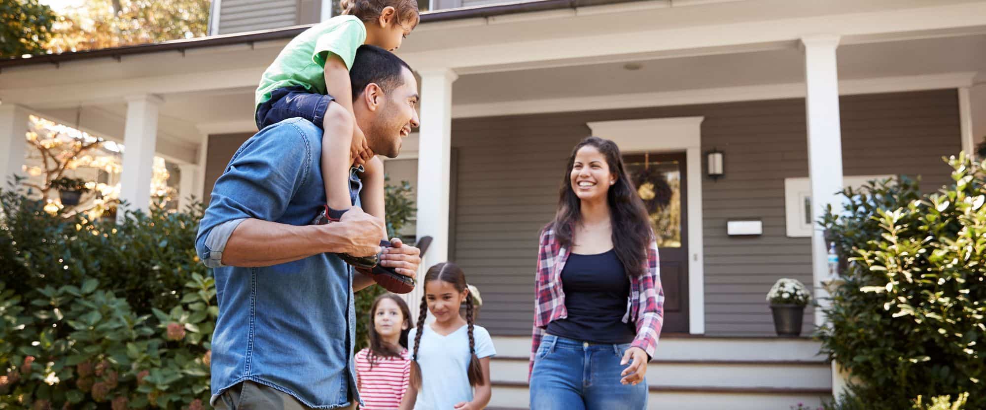 Roofers inspecting residential roof with family in front of house.