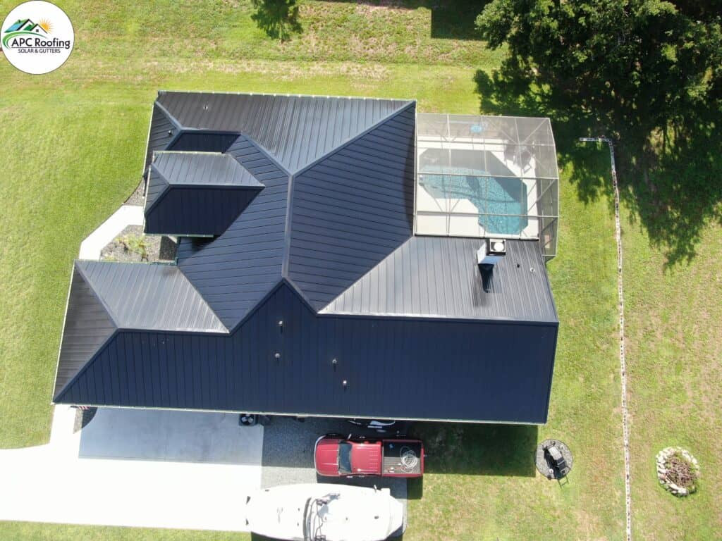 Aerial view of a modern house with a dark metal roof, a screened pool enclosure, and a red truck parked in the driveway.