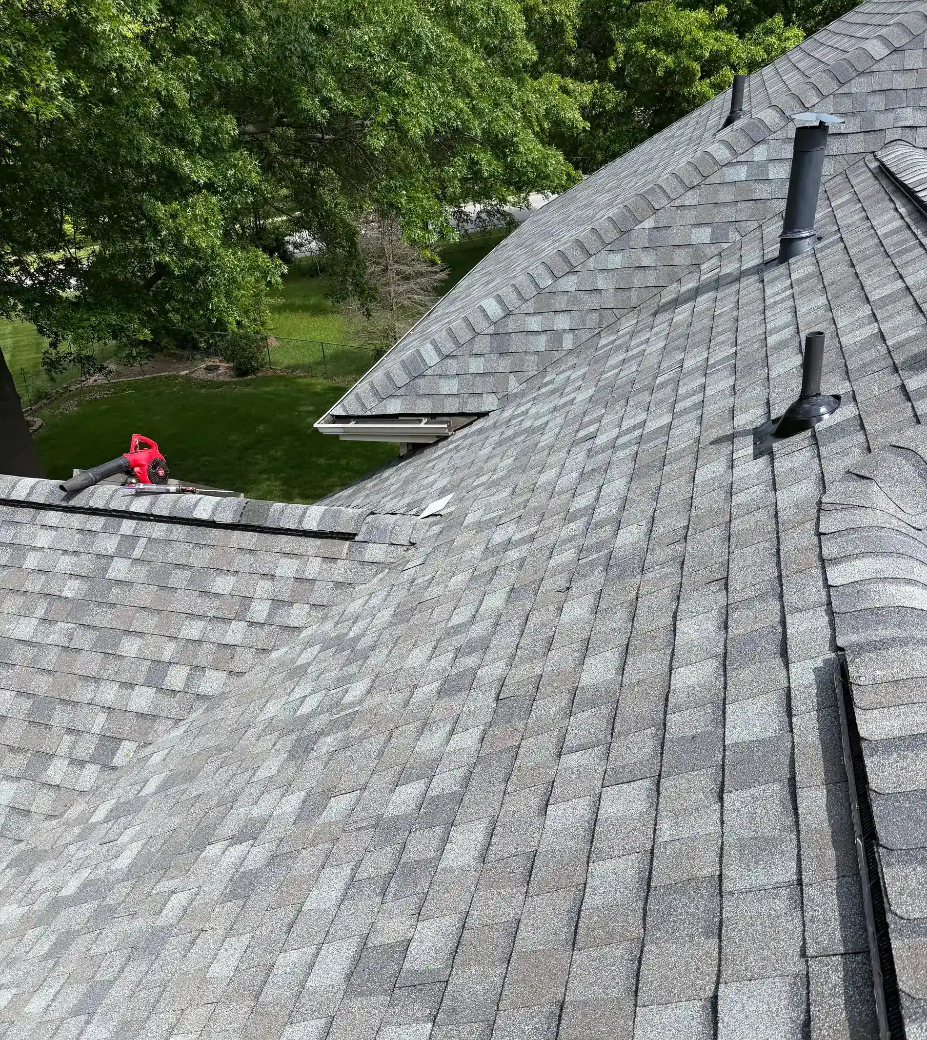 Roofers inspecting a gray shingle roof with multiple valleys and vents.