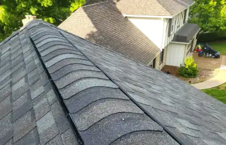 Roofers inspect a dark gray shingle roof with a steep pitch and valley intersection.