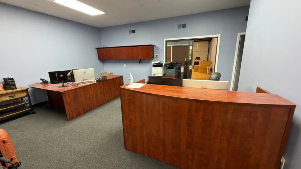 Office reception area with a curved wooden desk, computer, and printer against light blue walls.