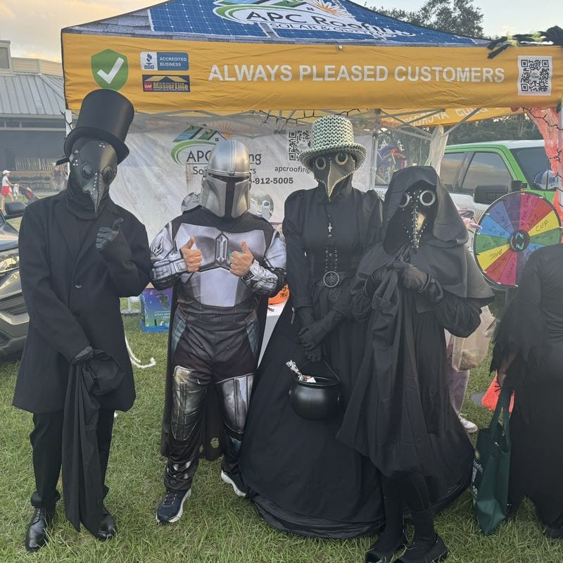 Guests in plague doctor and Mandalorian costumes at the APC Roofing Halloween booth